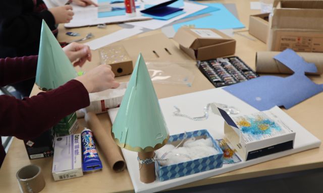 Na zdjęciu znajduje się konstrukcja przestrzenna pałacu Królowej Śniegu, który został wykonany z pudełek, kolorowego kartonu. W tle na stoliku znajdują się kartoniki i reszta przyborów.