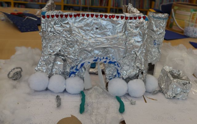 Na zdjęciu znajduje się pałac 3d wykonany z waty, cekinów i folii aluminiowej. Praca znajduje się na stole.