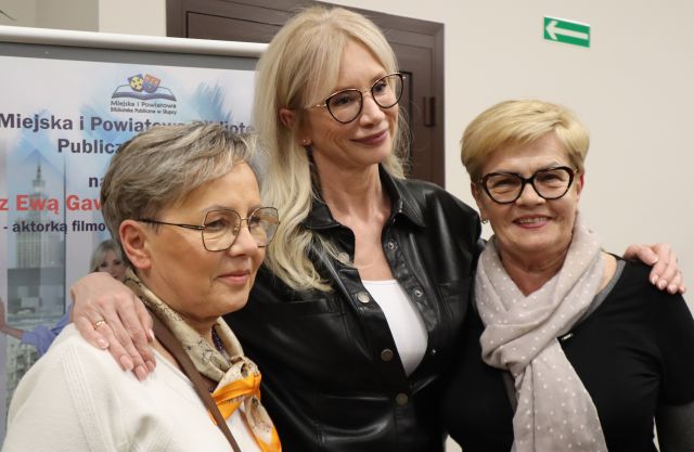 Na zdjęciu znajdują się dwie kobiety stojące do zdjęcia z Ewą Gawryluk. Za kobietami znajduje się plakat promujący spotkanie.