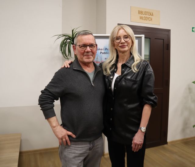 Na zdjęciu znajduje się mężczyzna stojący do zdjęcia z kobietą. Za nimi znajduje się plakat i kawałek zielonej rośliny.