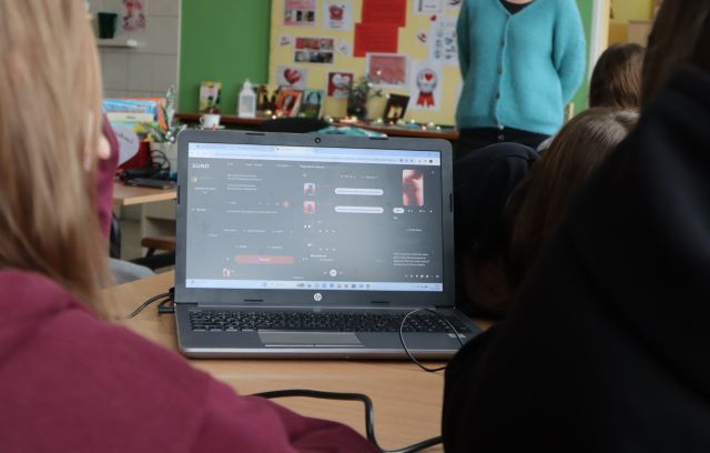 Na zdjęciu znajduje się laptop z wyświetloną aplikacją do tworzenia muzyki. Przed laptopem siedzą kobiety.