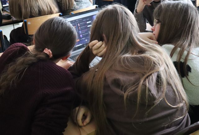 Na zdjęciu znajdują się trzy dziewczyny siedzące i nachylające się nad laptopem. Zdjęcie zostało wykonane od tyłu.