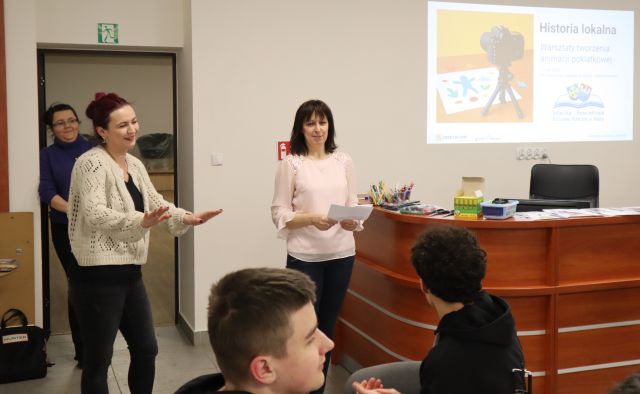 Na zdjęciu znajdują się dwie kobiety, za nimi w drzwiach stoi kobiet, a przed znajduje się dwóch nastolatków. Po prawej stronie na ścianie wyświetlana jest prezentacja dotycząca animacji poklatkowej.