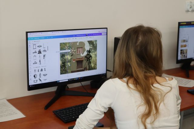 Na zdjęciu znajduje się dziewczyna siedząca przy komputerze, na którym wykonuje kolaż dotyczący miasta. Zdjęcie zostało wykonane od tyłu.