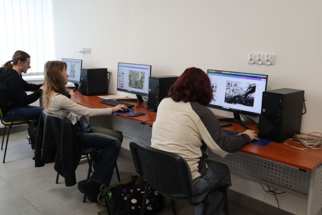 Na zdjęciu znajdują się dwie dziewczyny i jeden chłopak przy komputerach, na których wykonują kolaż. Warsztaty odbywają się w sali komputerowej.