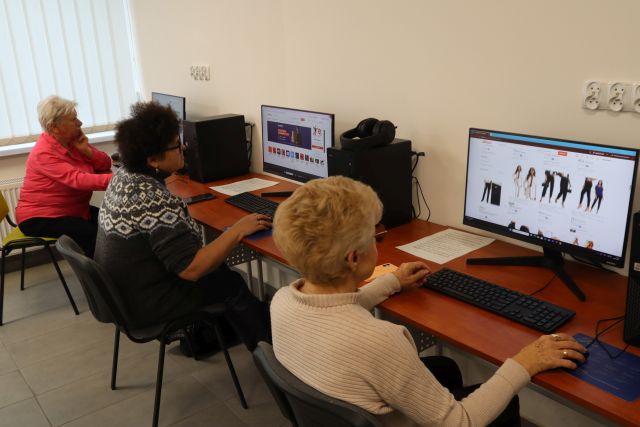 Na zdjęciu znajdują się trzy kobiety przy komputerach i przeglądają sklepy internetowe. Warsztaty odbywają się w sali komputerowej.