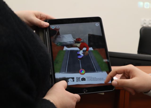 Na zdjęciu znajduje się tablet trzymany przez kobietę, na którym znajduje się ożywiony obrazek.