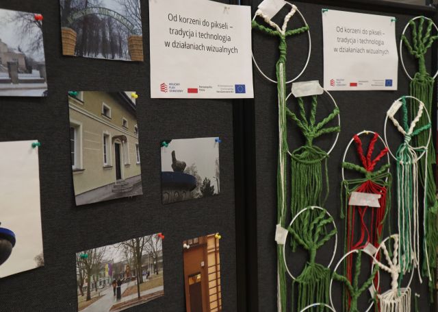 Na zdjęciu znajdują się zdjęcia powieszone na czarnej tablicy oraz drzewa szczęścia na kole po prawej, Do góry wiszą dwie kartki a nazwą projektu.