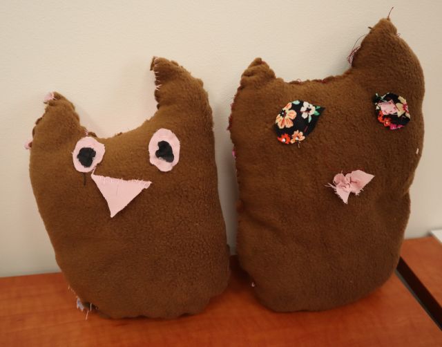 Na zdjeciu znajdują się dwie uszyte brązowe sowy obok siebie. Maskotki znajduja sie na drewnianym stole.