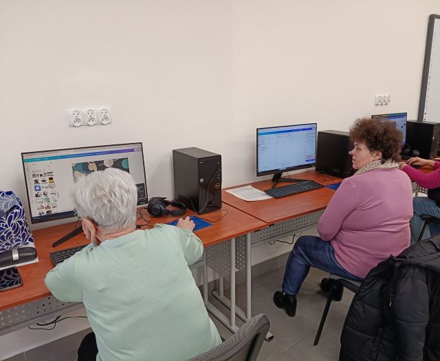 Na zdjęciu znajdują się dwie kobiety siedzące przy komputerach w sali komputerowej.