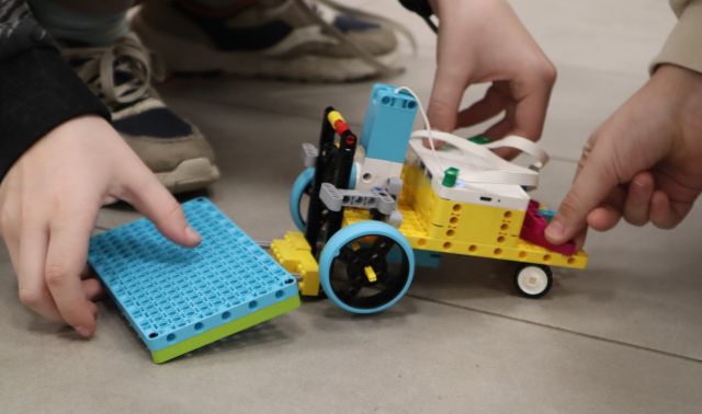 Na zdjęciu znajduje się samochód z LEGO, który podnosi klocki i jest trzymany przez chłopca. 