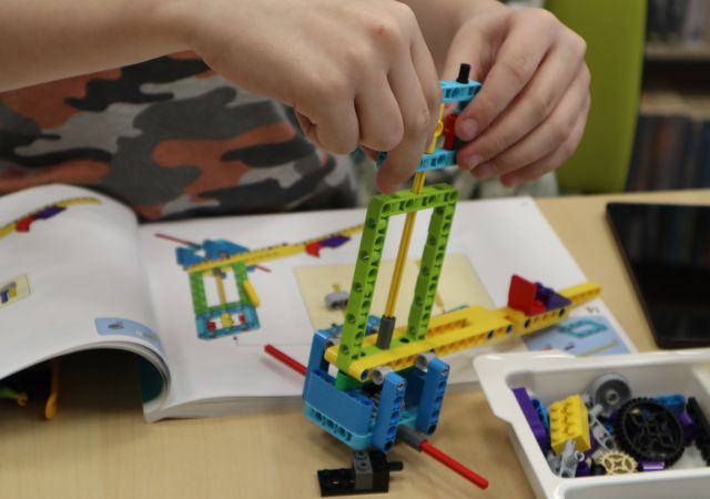 Na zdjęciu znajduje się chłopiec budujący z LEGO, przed nim na stoliku leży instrukcja.