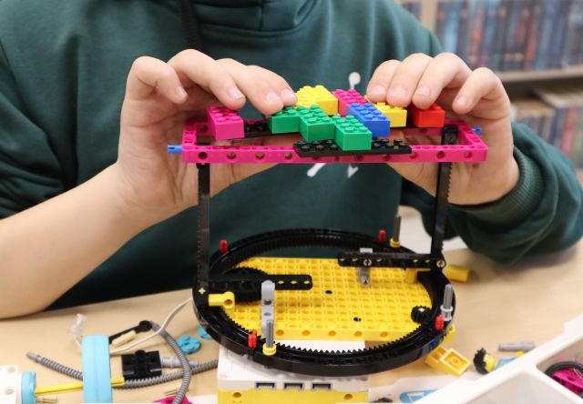 Na zdjęciu znajduje się okrągła konstrukcja z LEGO na stoliku budowana przez chłopca.