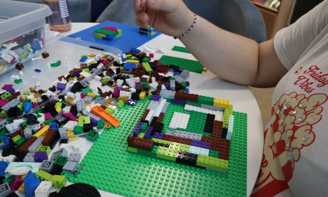 Na zdjęciu znajdują się klocki LEGO na stole, które układa dziewczynka.