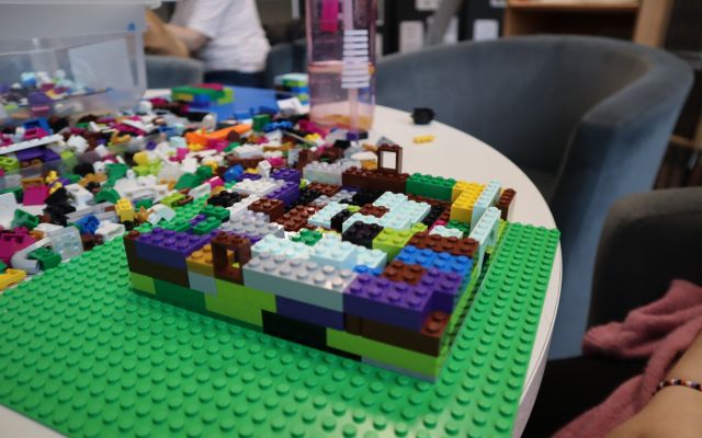 Na zdjęciu znajduje się leżąca na stole klocki LEGO oraz kwadratowa budowla.