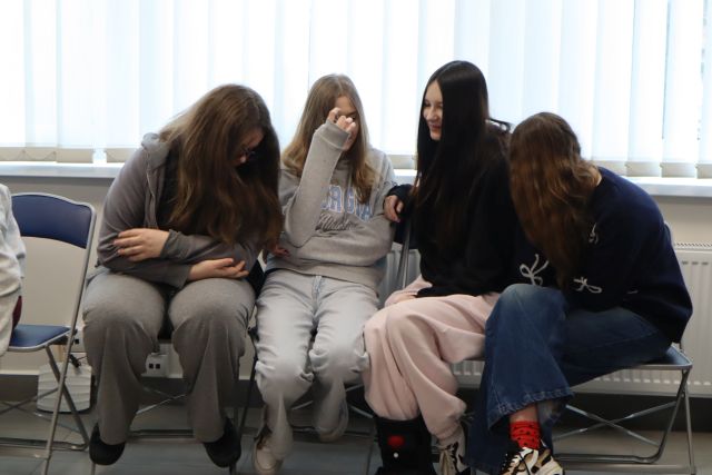 Na zdjęciu znajduje się czwórka dziewczyn siedząca na krzesłach i dyskutująca, w tle znajdują się okna.