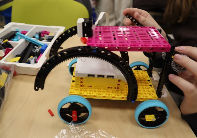 Na zdjęciu znajduje się zbudowany z klocków LEGO samochód leżący na stole, dookoła znajdują się klocki w opakowaniu.