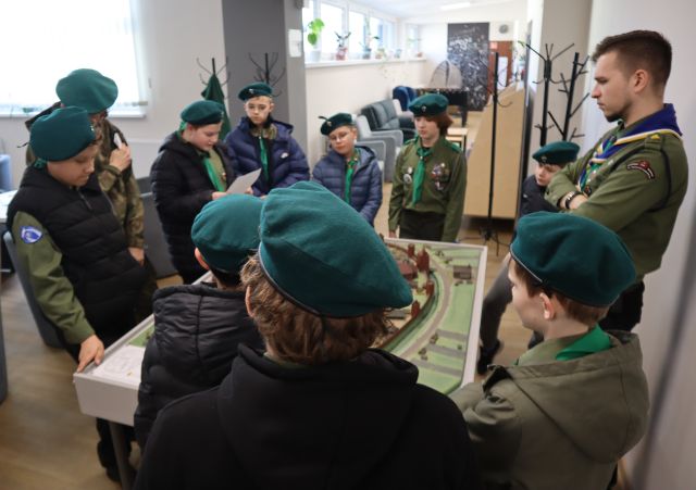 Na zdjęciu znajdują się harcerze, którzy stoją dookoła makiety miasta Słupca, która znajduje się na holu biblioteki.