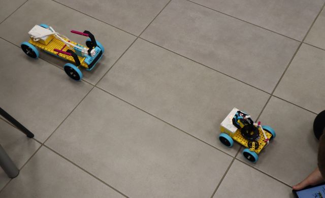 Na zdjęciu znajdują się dwa robotyczne samochody zbudowane z LEGO i leżą na podłodze.