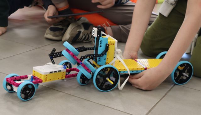 Na zdjęciu znajdują się dwa roboty z LEGO, robot po prawej jest zdecydowanie większy i jest trzymany rękoma.