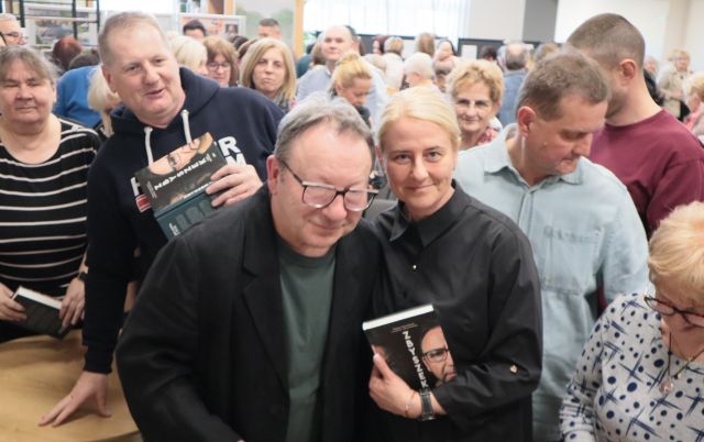 Na zdjęciu znajduje się mężczyzna oraz kobieta z książką i stoją wspólnie do zdjęcia. W tle znajdują się ludzie.