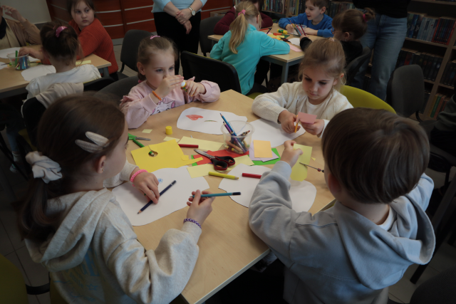 Na zdjęciu znajduje się czwórka przedszkolaków przy stoliku i kolorują papierowe słoiczki.