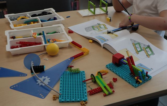 Na zdjęciu znajdują się klocki LEGO na stoliku wraz z instrukcją według której chłopiec składa klocki.