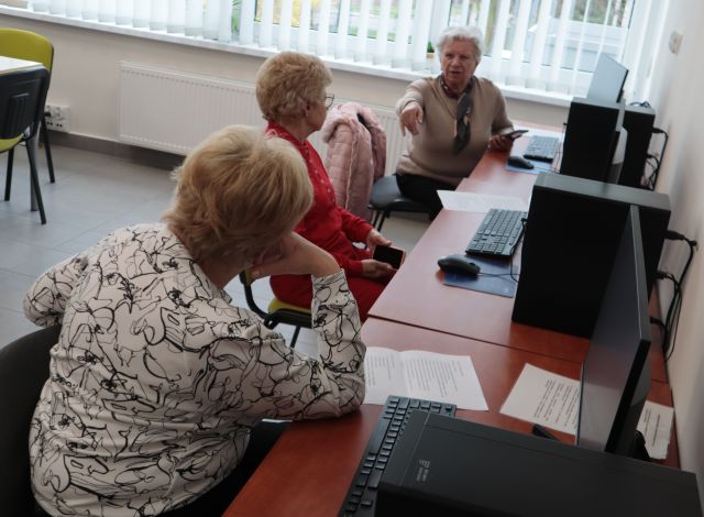 Na zdjęciu znajdują się trzy kobiety przy komputerach, które ze sobą rozmawiają. Zajęcia odbywają się w sali komputerowej.