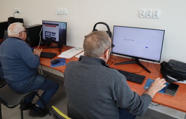 Na zdjęciu znajduje się dwóch mężczyzn, którzy wyszukują informacji w komputerach, przy których siedzą.