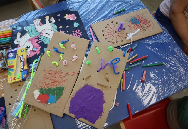 Na zdjęciu znajdują się trzy kartonowe prostokąty, na których narysowana i ozdobiona jest doniczka oraz w dziurki przeciągnięte są druciki kreatywne. Prace leżą na niebieskim stoliku, który jest owinięty streczem , dookoła leżą kredki.