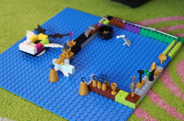 Na zdjęciu znajduje się niebieska podkładka, na której zbudowane jest kwadratowe pomieszczenie. Praca znajduje się na dywanie.