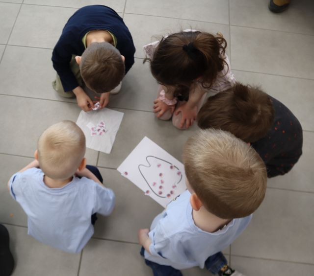 Na zdjęciu znajduje się piątka dzieci na podłodze, przed nimi leży kartka z narysowanym zębem oraz kartka na której chłopiec liczy ile bakterii udało im się złapać. Zdjęcie zostało wykonane od óry.