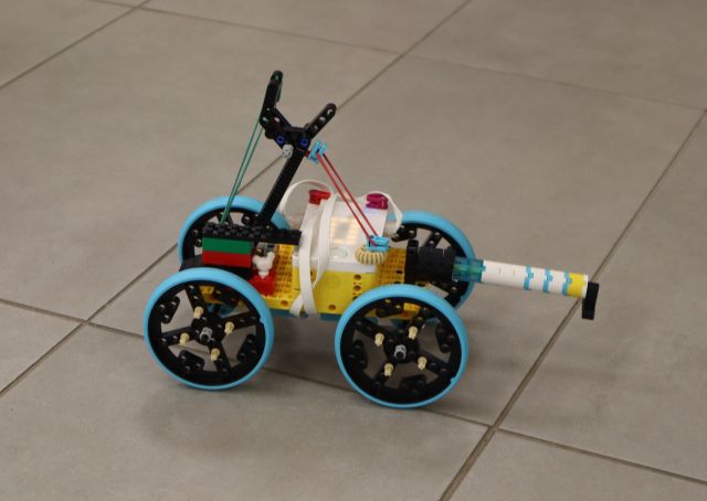 Na zdjęciu znajduje się samochód zbudowany z klocków LEGO, który stoi na podłodze. Na pojeździe znajduje się wyrzutnia.