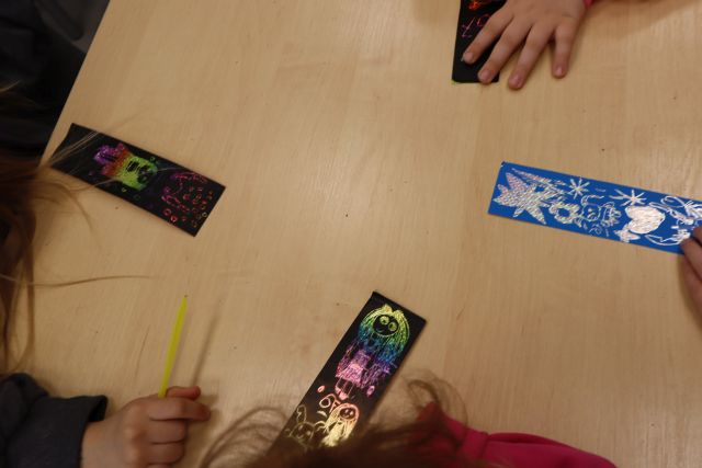 Na zdjęciu znajduje się stół oraz cztery kolorowe zakładki wykonywane przez dzieci z wydrapywanki.