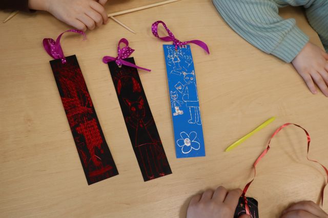 Na zdjęciu znajdują się trzy zakładki do książek, dwie czarno czerwone, jedna niebiesko srebrna wykonane z wydrapywanek, posiadają również zawieszkę ze wstążki. Prace leżą na stole.