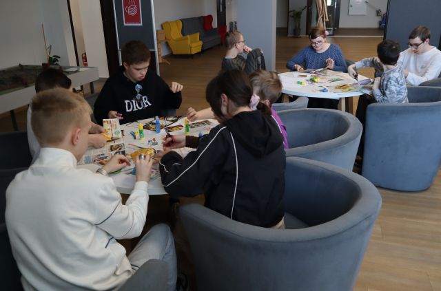 Na zdjęciu znajduje się młodzież przy dwóch stolikach i robią kolaże na dzień ziemi. Warsztaty odbywają się na holu biblioteki.