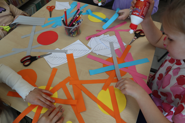 Na zdjęciu znajduje się stolik przy którym dzieci tworzą z kolorowych kartek kwiatki.