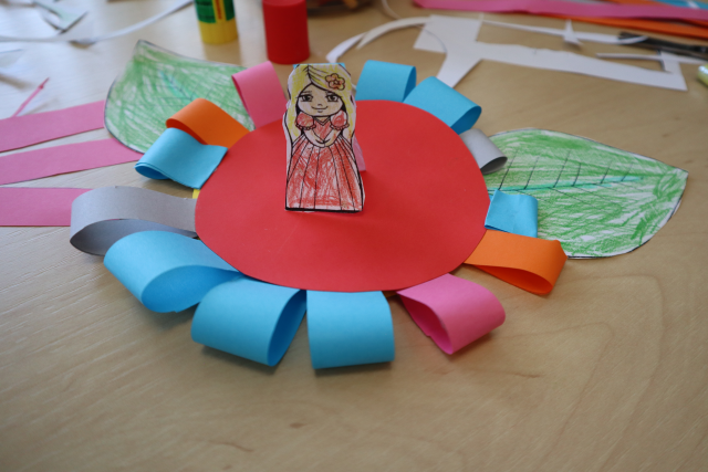 Na zdjęciu znajduje się leżąca na stole praca z papieru przedstawiająca Calineczkę na kwiatku, w tle znajdują się resztki materiałów.