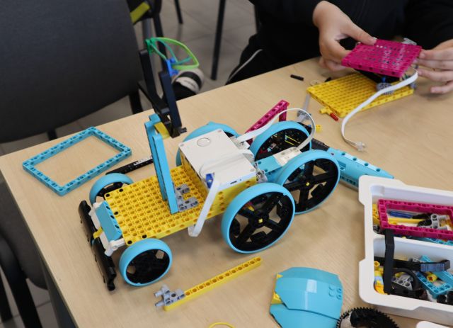 Na zdjęciu znajduje się stolik, na którym leżą klocki LEGO oraz ułożony z nich samochód. Przy stoiku stoi krzesło.
