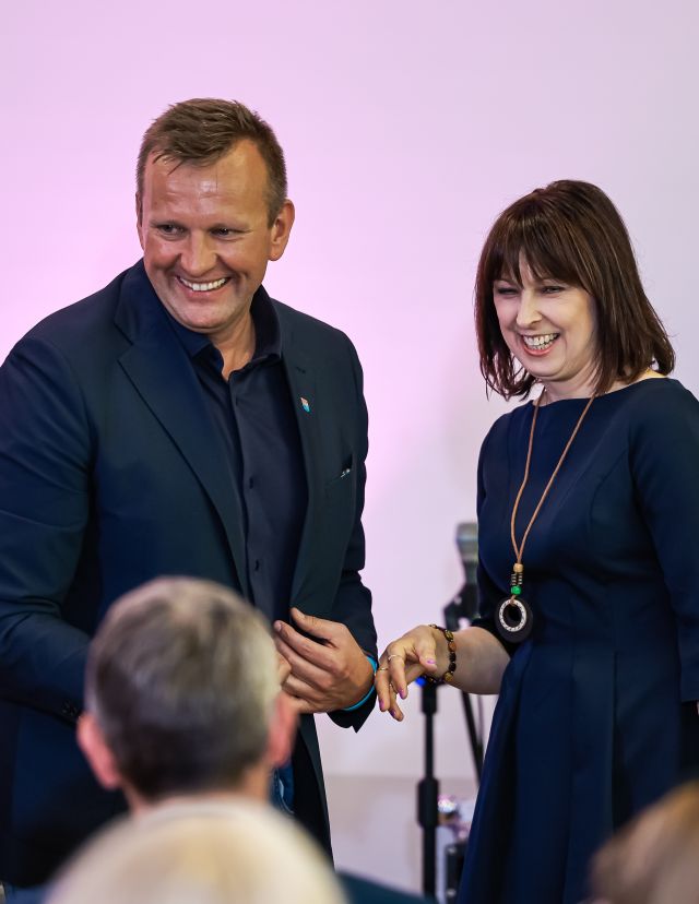Na zdjęciu znajduje się kobieta wraz z mężczyzną i się śmieją, przed nimi siedzi mężczyzna.