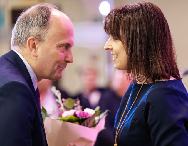 Na zdjęciu znajduje się mężczyzna wręczający kobiecie kwiaty. Zdjęcie zostało wykonane od boku.