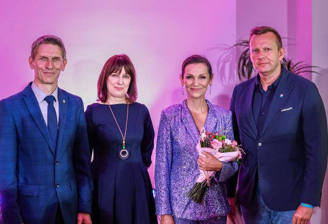 Na zdjęciu znajduje się dwóch mężczyzn oraz dwie kobiety i stoją do wspólnego zdjęcia, jedna z kobiet trzyma w ręku kwiaty.