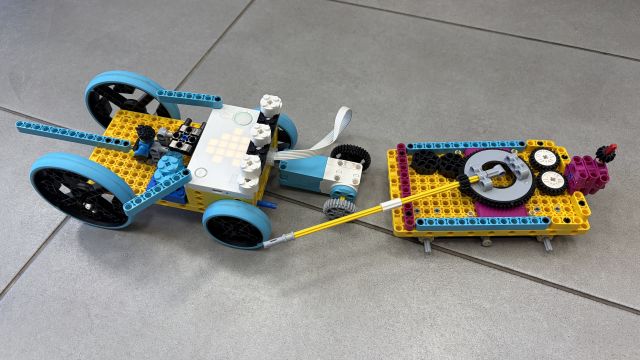 Na zdjęciu znajduje się zbudowany z klocków LEGO pojazd, imitujący czołg, który ma przymocowaną do tyłu przyczepę również z klocków LEGO. Pojazdy znajdują się na kafelkach.