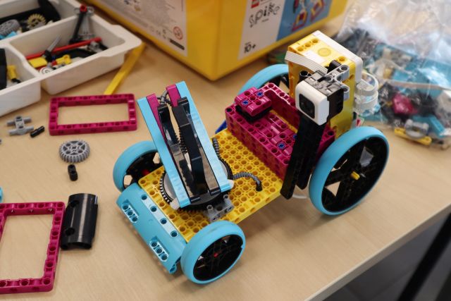 Na zdjęciu znajduje sie samochód zbudowany z klocków LEGO, który stoi na stole a dookoła niego znajdują się klocki LEGO.