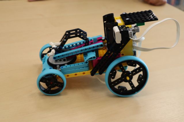 Na zdjęciu znajduje się samochód z LEGO leżący na stole, przednie koła ma mniejsze.