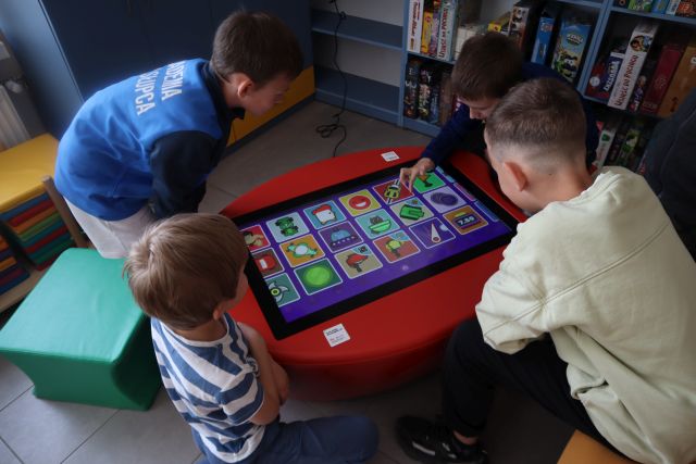 Na zdjęciu znajduje się czwórka chłopców przy stoliku multimedialnym, przy którym grają w gry edukacyjne.