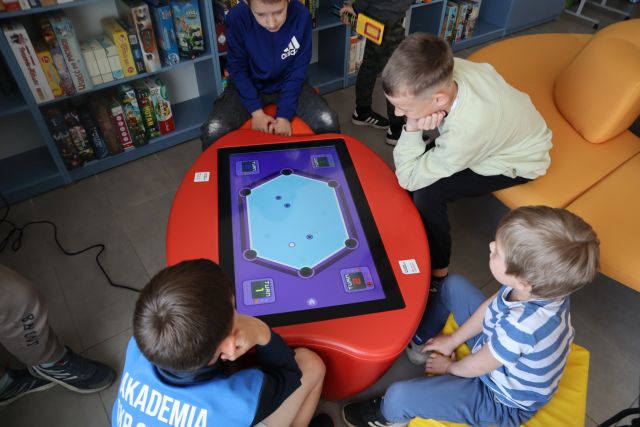 Na zdjęciu znajduje się czwórka chłopców, którzy grają w gry edukacyjne na stoliku interaktywnym. 