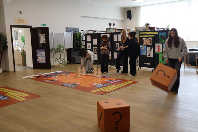 Na zdjęciu znajduje się młodzież grająca w grę wielkoformatową na holu biblioteki.