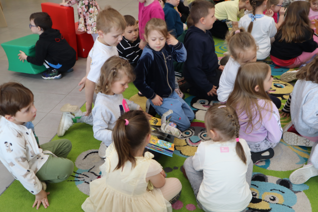 Na zdjęciu znajdują się przedszkolaki oglądające na dywanie książkę. Zdjęcie zostało wykonane od góry.