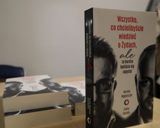 Na zdjęciu znajdują się książki na stoliku, trzy książki leżą, a jedna stoi i widoczna jest okładka książki. Na okładce znajdują się twarze dwóch mężczyzn i tytuł ,,Wszystko, co chcielibyście wiedzieć o Żydach, ale za bardzo baliście się zapytać.